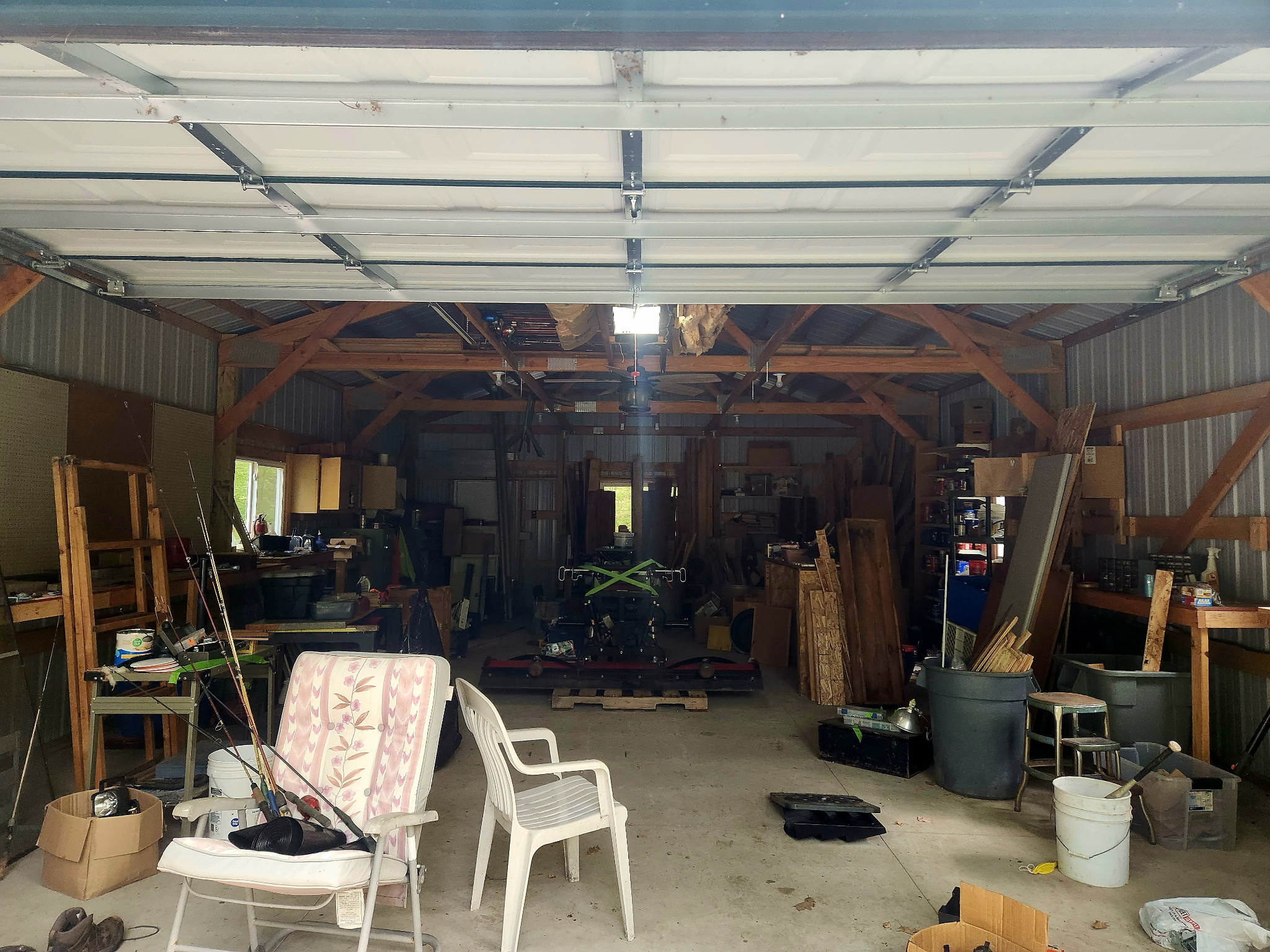 Pole barn interior before the cleanout, crowded with stacked lumber, chairs, buckets, bins and stored equipment.